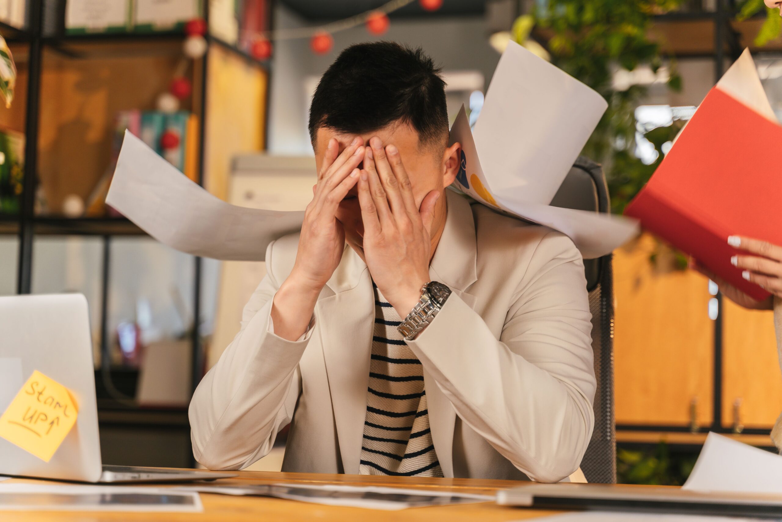 Man stressed over documents, laptop with "Start Up" note, business policy and procedure