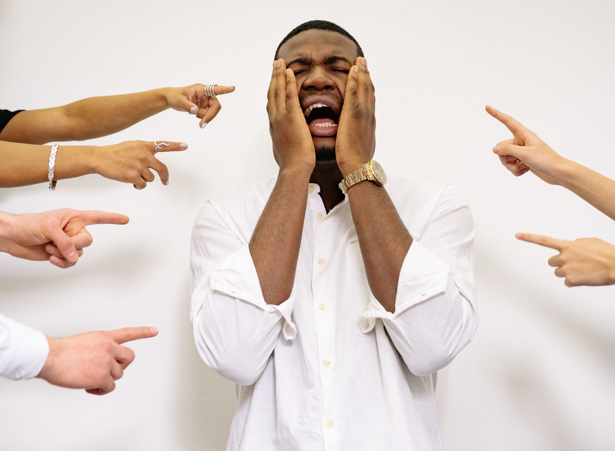 Man overwhelmed by pointing fingers, symbolizing bullying and harassment.