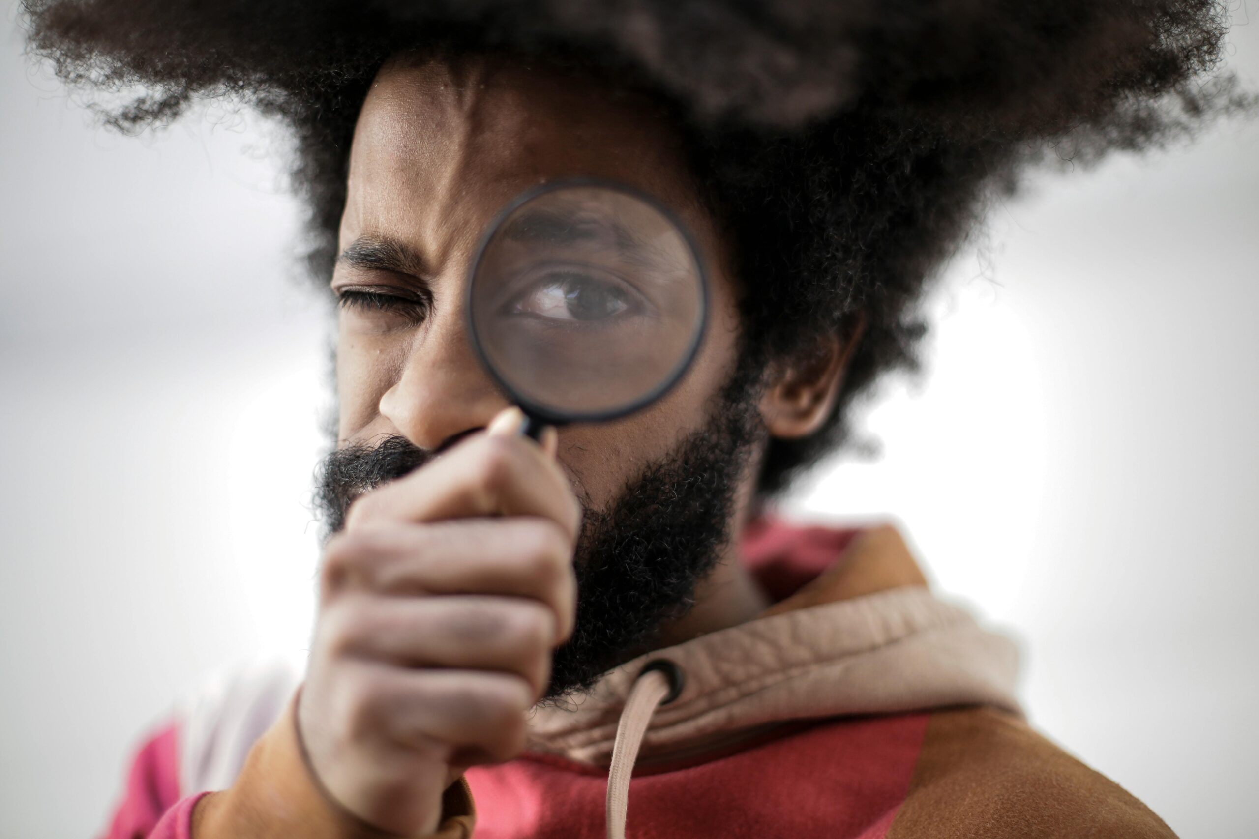 Man with afro and beard uses magnifying glass, symbolizing open disclosure and scrutiny.