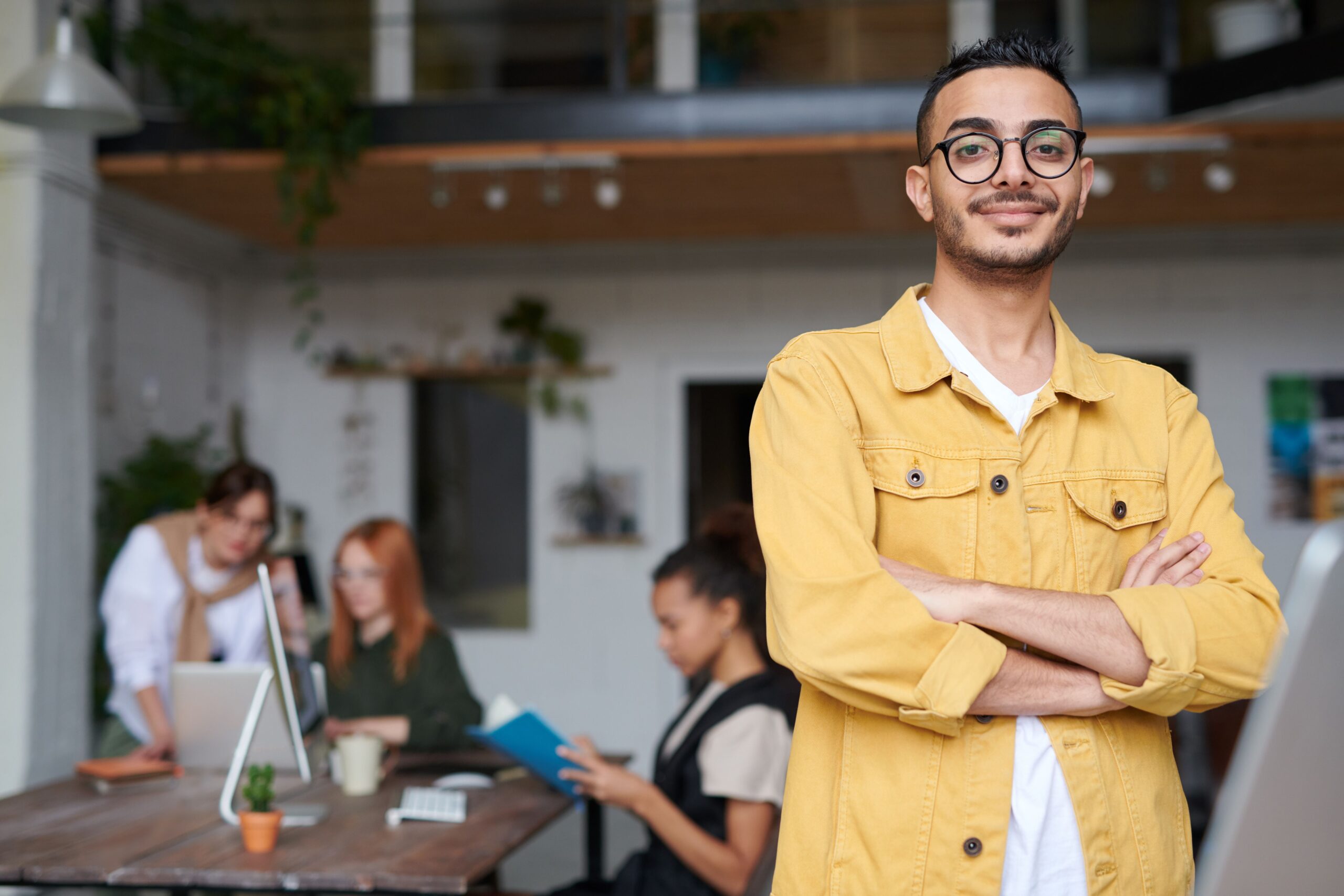 Man in yellow jacket with arms crossed in modern office with team working