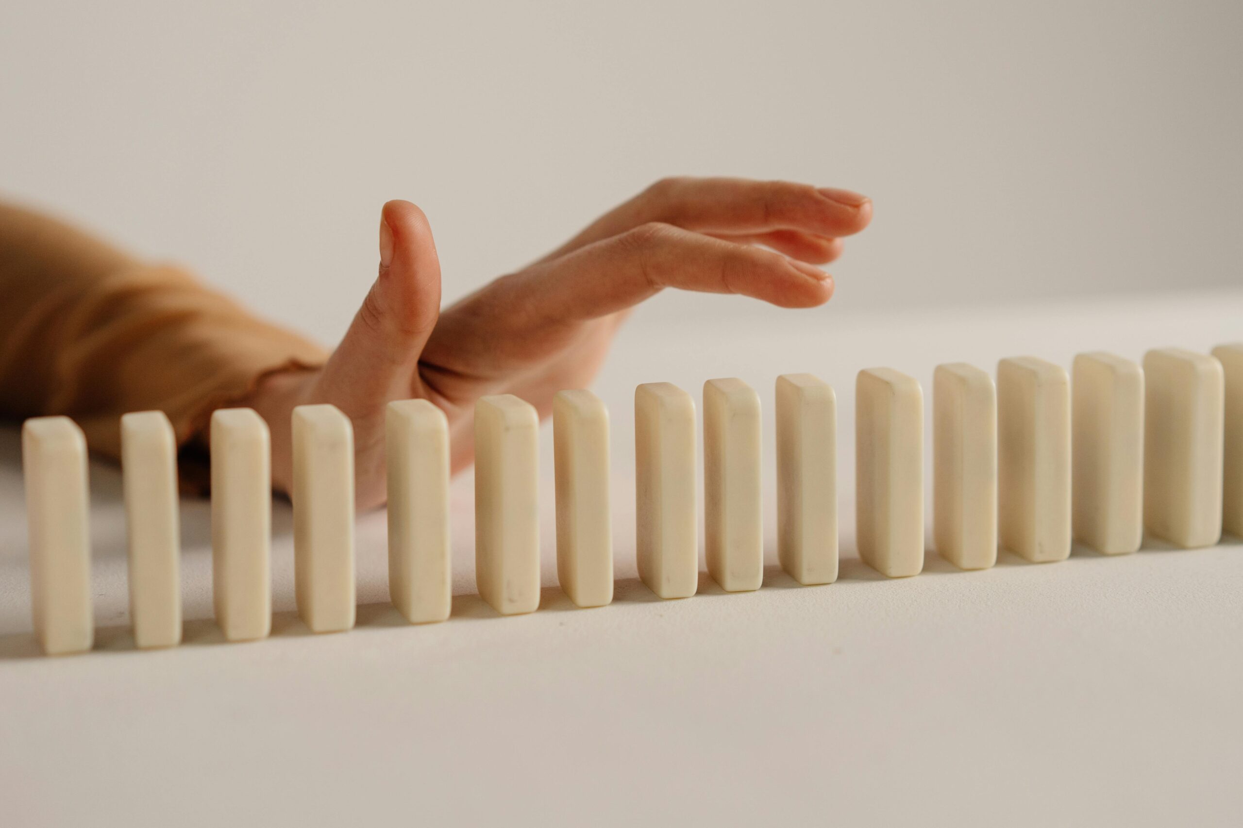 Hand stopping dominoes, symbolizing risk management with policies and procedures.