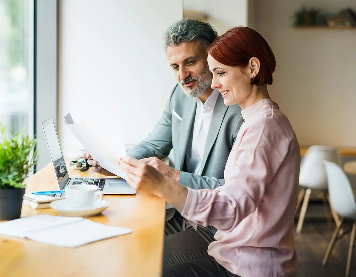 Business professionals reviewing documents at a cafe table with laptop and coffee