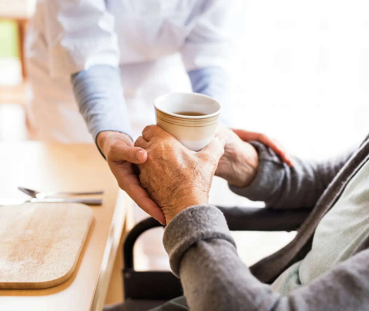 A helper assists someone to hold a cup of coffee