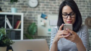Woman in glasses using smartphone at desk, discussing mobile device policies for social services.